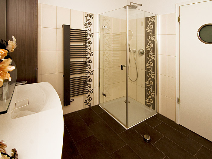 Badezimmer mit anthrazitfarbenen Fliesen und Handtuchheizung, sowie cremefarbenen Wandfliesen und floralen Elementen