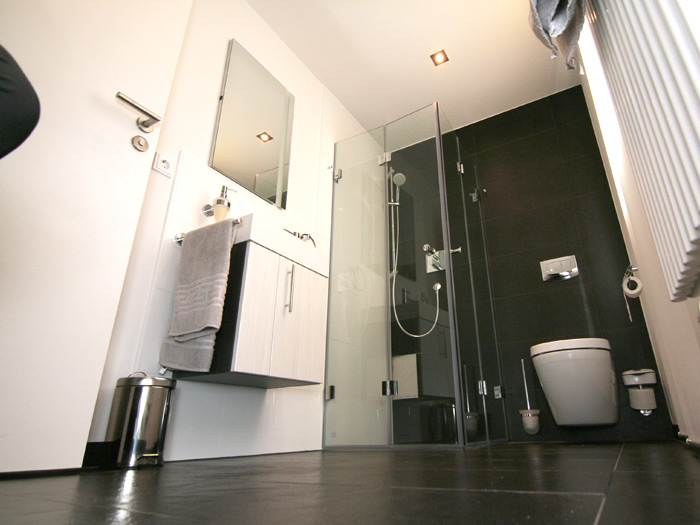Ebenerdige Dusche in einem Badezimmer mit schwarzen, großformatigen Bodenfliesen, weißen Wandfliesen und einer schwarz gefliesten Wand.