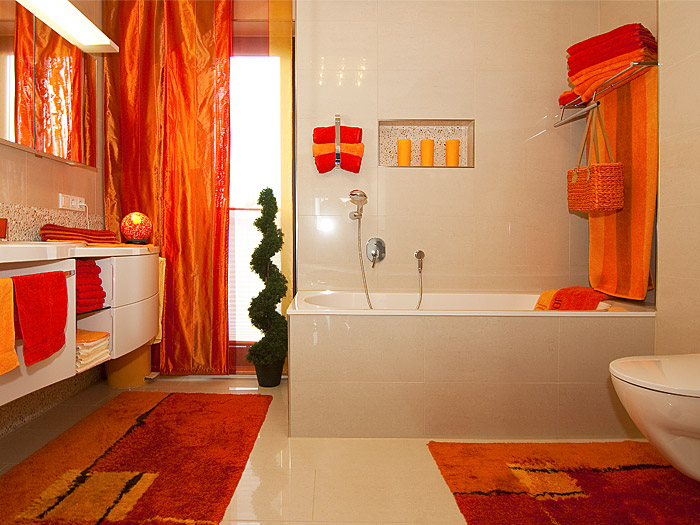 Saniertes Badezimmer mit Badewanne mit hellen Wandfliesen und hellen Bodenfliesen und orangefarbener Deko.