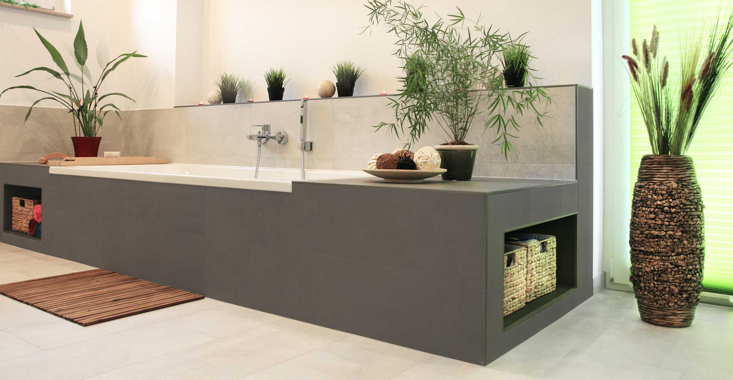 Eine rechteckige Badewanne eingefasst in Trockenbauelementen in grau und beige mit integrierten Ablageflächen.
