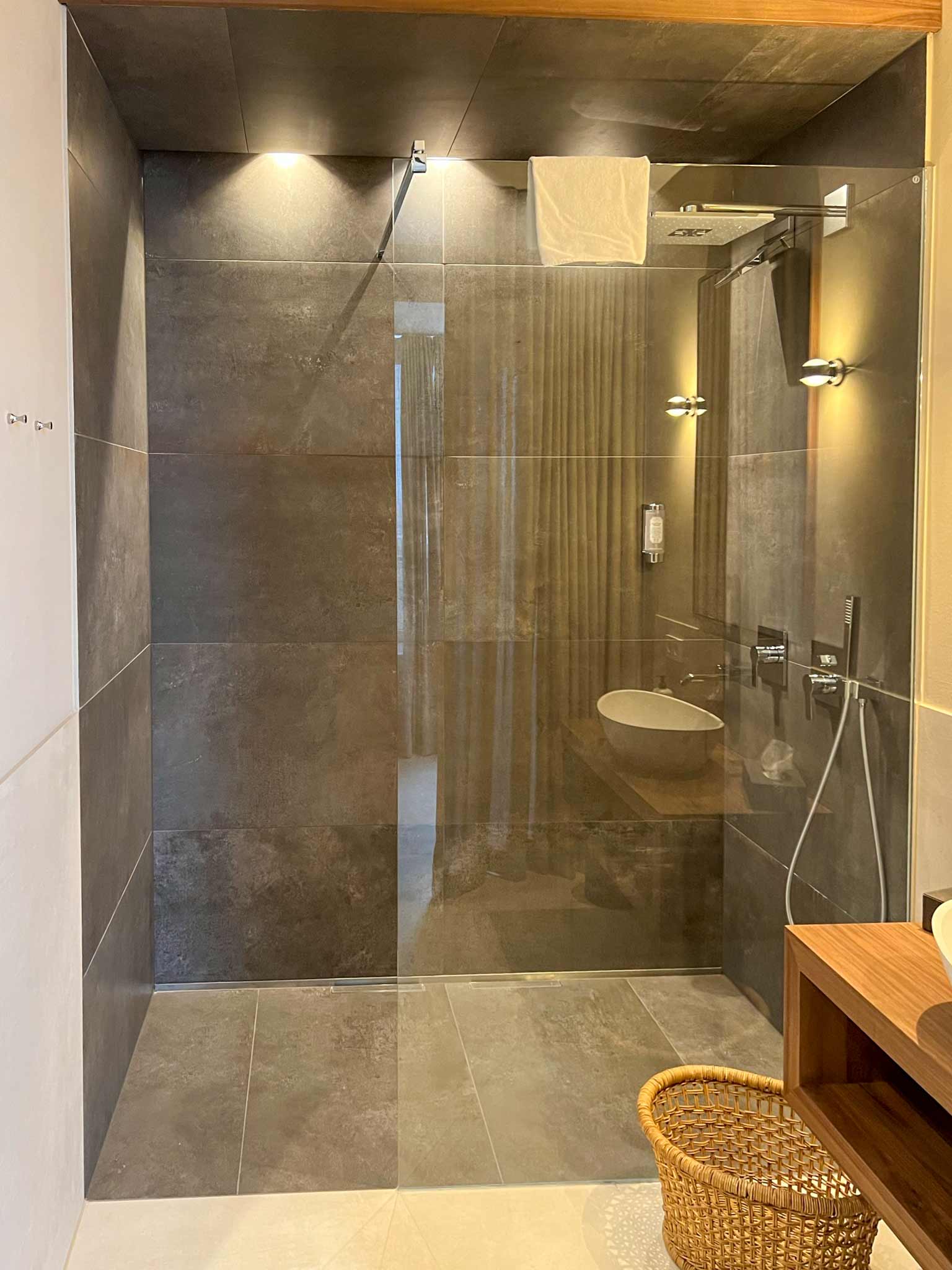 Bodengleiche Dusche mit dunklen großformatige bzw. XXL-Fliesen in einem hell gefliesten Badezimmer.
