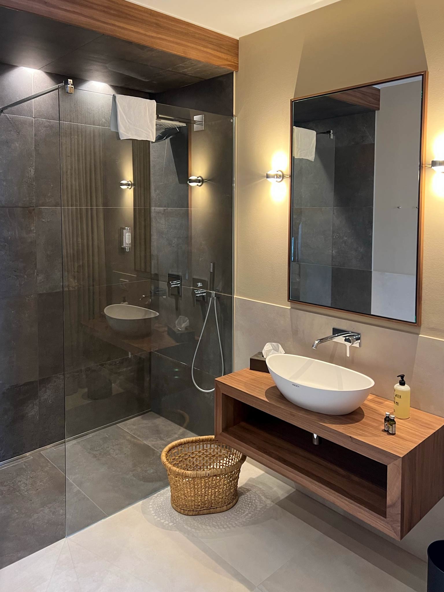 Modernes Badezimmer mit dunklen Wandfliesen, Holz-Waschtisch und weißem Keramik-Aufsetzwaschbecken